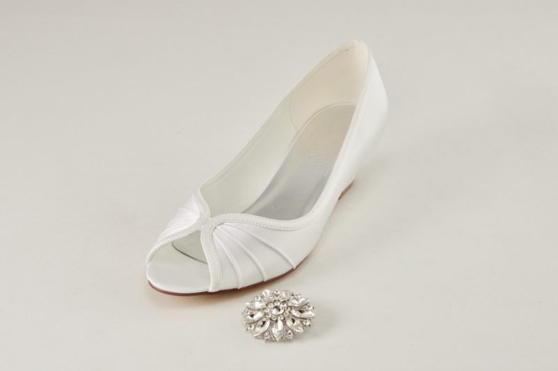 Bílé svatební boty na nízkém klínku s otevřenou špičkou. Na nártu odepínací kamínková spona.